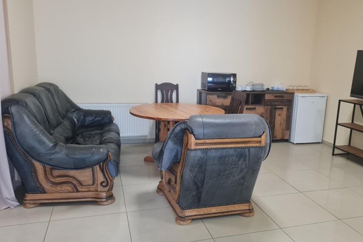 A living room with a sofa, a chair, a coffee table, a television on a stand, and a small refrigerator.
