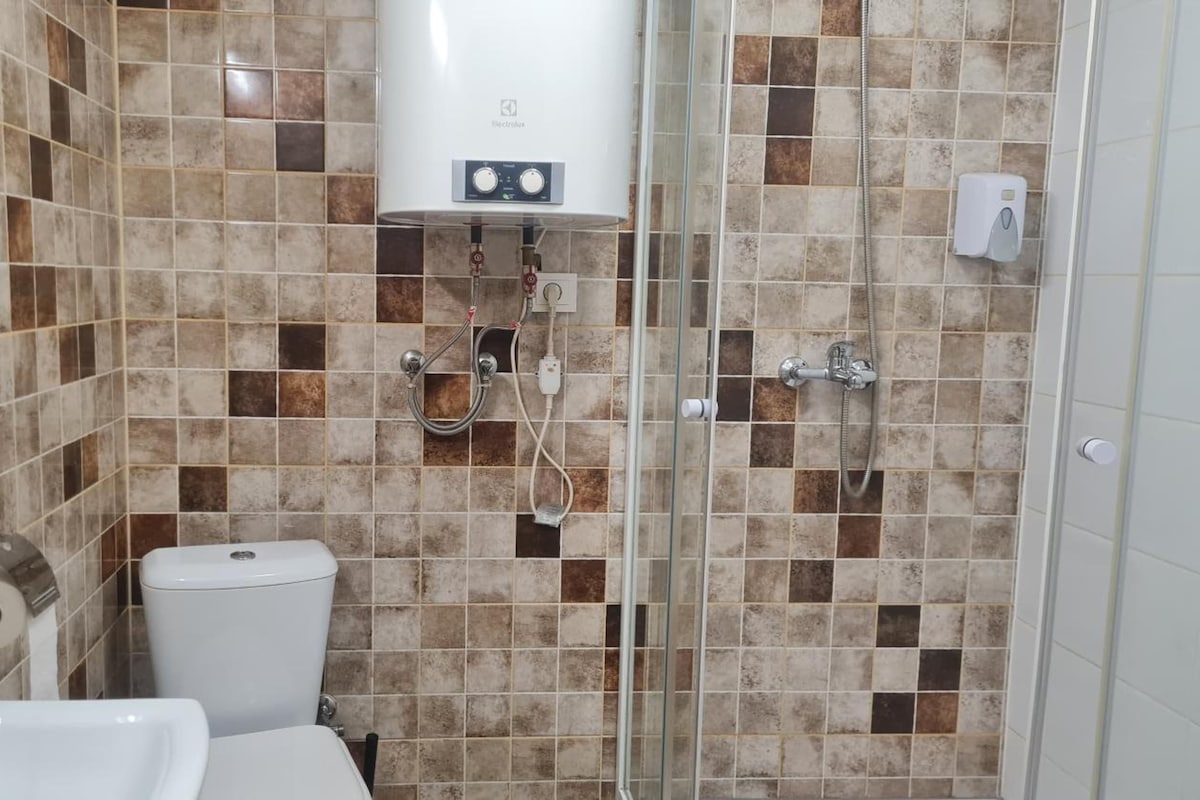A bathroom with a toilet, sink, shower, and a water heater.