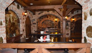 Interior de restaurante con paredes de piedra, vigas de madera y un mural. Las mesas están dispuestas con cubiertos y condimentos.