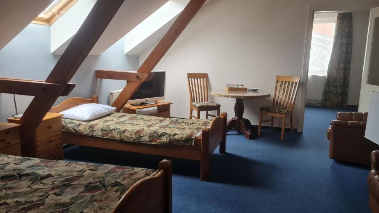 A room with a sloped ceiling, a bed, a desk, a chair, and a small table.