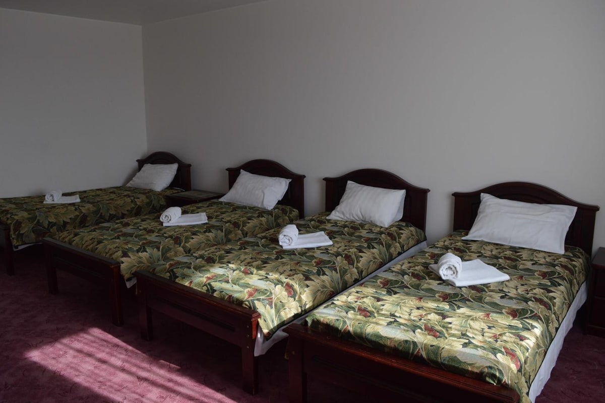 A hotel room with three single beds, each with a floral bedspread and a white pillow.