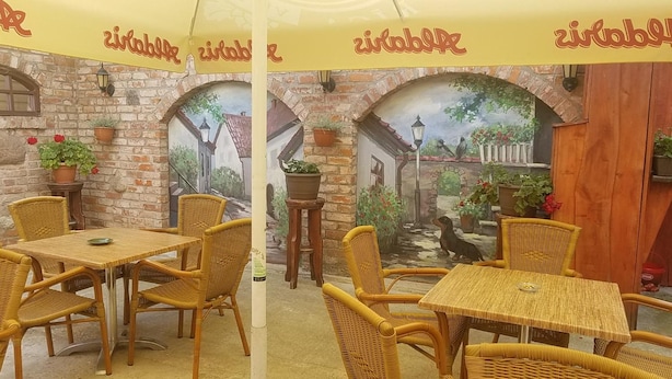 A restaurant with outdoor seating, wicker furniture, and a mural of a village scene. - Hotel Tukums (Tukums)