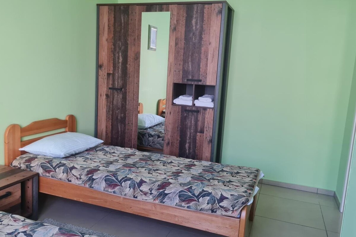 Una cama individual con colcha estampada, cabecera de madera, mesita de noche y armario con espejo.