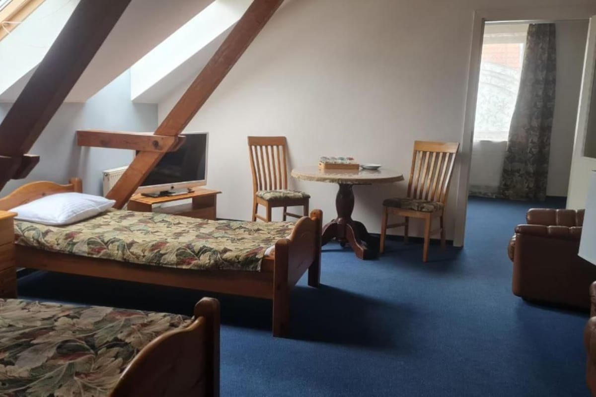 A room with a sloped ceiling, a bed, a desk, a chair, and a small table.