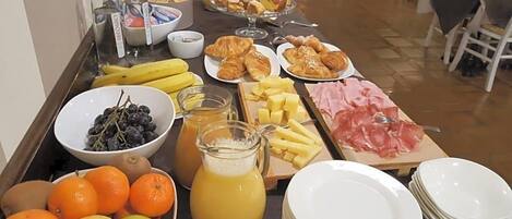 Une table de buffet proposant une variété d’aliments, notamment des fruits, des pâtisseries et du fromage.