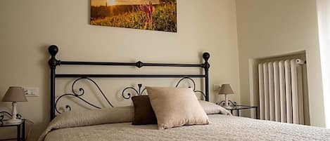 Una cama bien hecha con cabecera, dos lámparas de noche y un cuadro colgado en la pared.