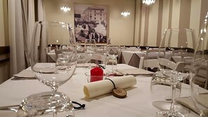 Un comedor con mesas dispuestas para una comida, con cristalería transparente y un centro de mesa con una vela roja.
