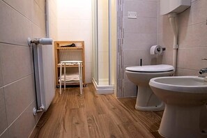 Un baño con inodoro, bidé y un estante con toallas.