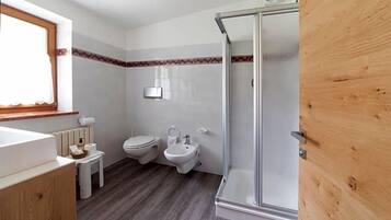 Ein Badezimmer mit Dusche, Toilette, Bidet und einem kleinen Tisch mit Pflegeprodukten.