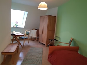 A room with a bed, a desk with a chair, a wardrobe, and a window with natural light.