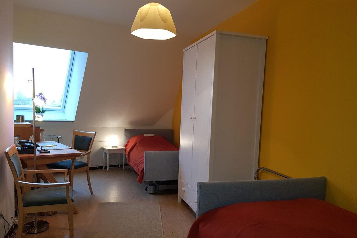 A room with a desk, chair, bed, wardrobe, and a window with a view.