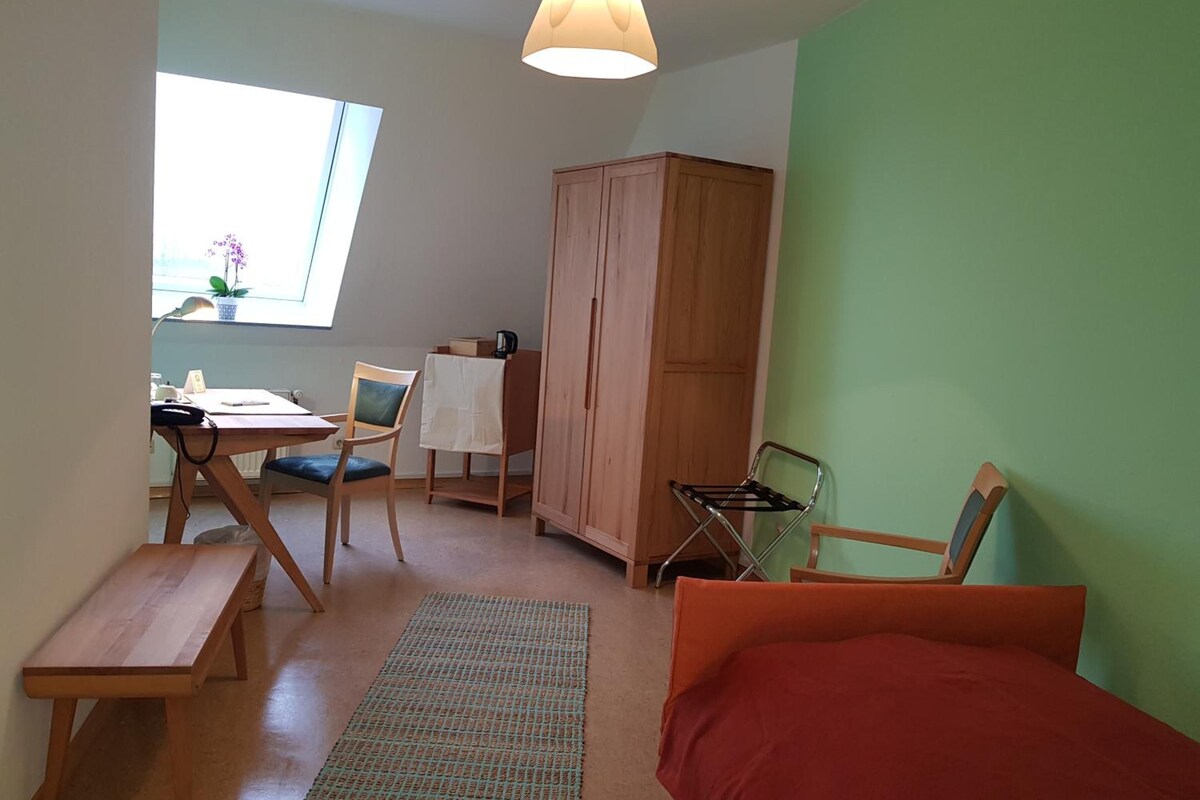 A room with a bed, a desk with a chair, a wardrobe, and a window with natural light.