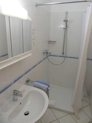 A bathroom with a sink, mirror, shower, and towel rack.