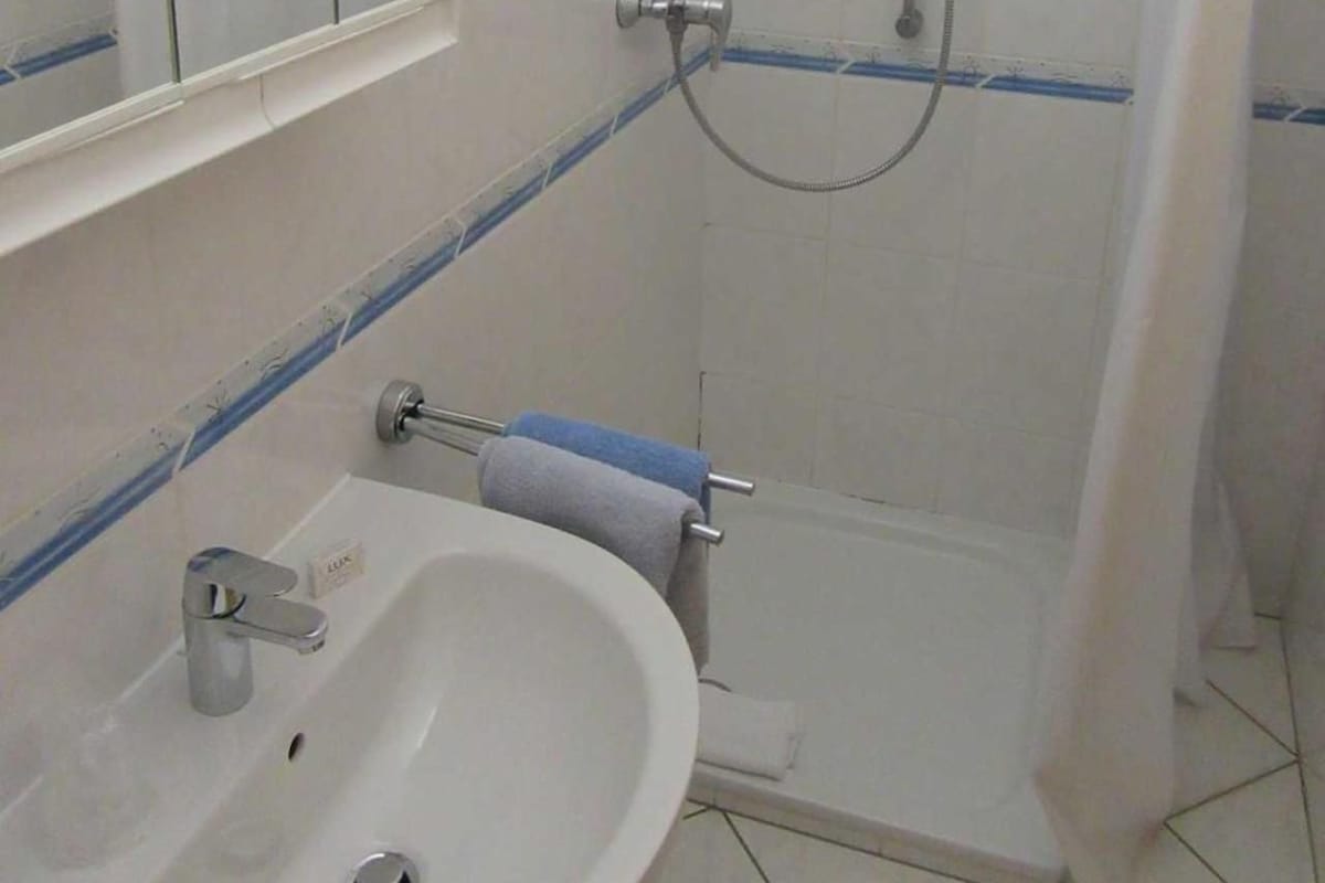A bathroom with a sink, mirror, shower, and towel rack.