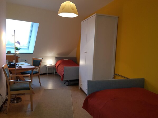 A room with a desk, chair, bed, wardrobe, and a window with a view.