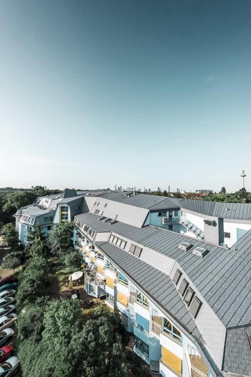A multi-story residential building with a curved roof design, balconies, and a parking area with cars.