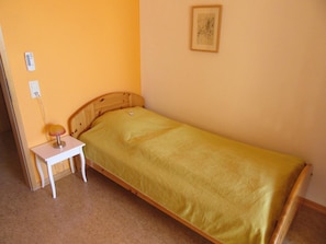 A single bed with a wooden headboard, a bedside table with a lamp, and a framed picture on the wall.