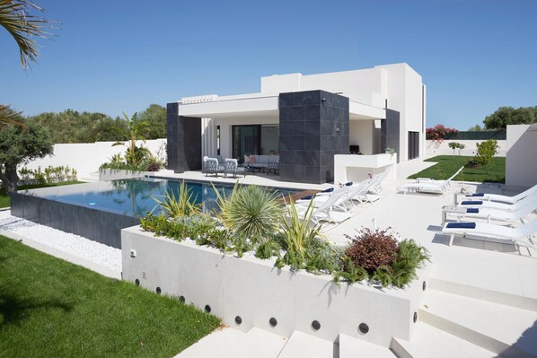 Et moderne hus med swimmingpool, udendørs møbler og en velplejet have.