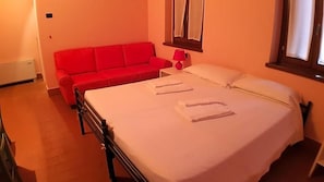 A room with a bed, a red sofa, and a window. - Ostello Molino Di Basso (Torre Pallavicina)