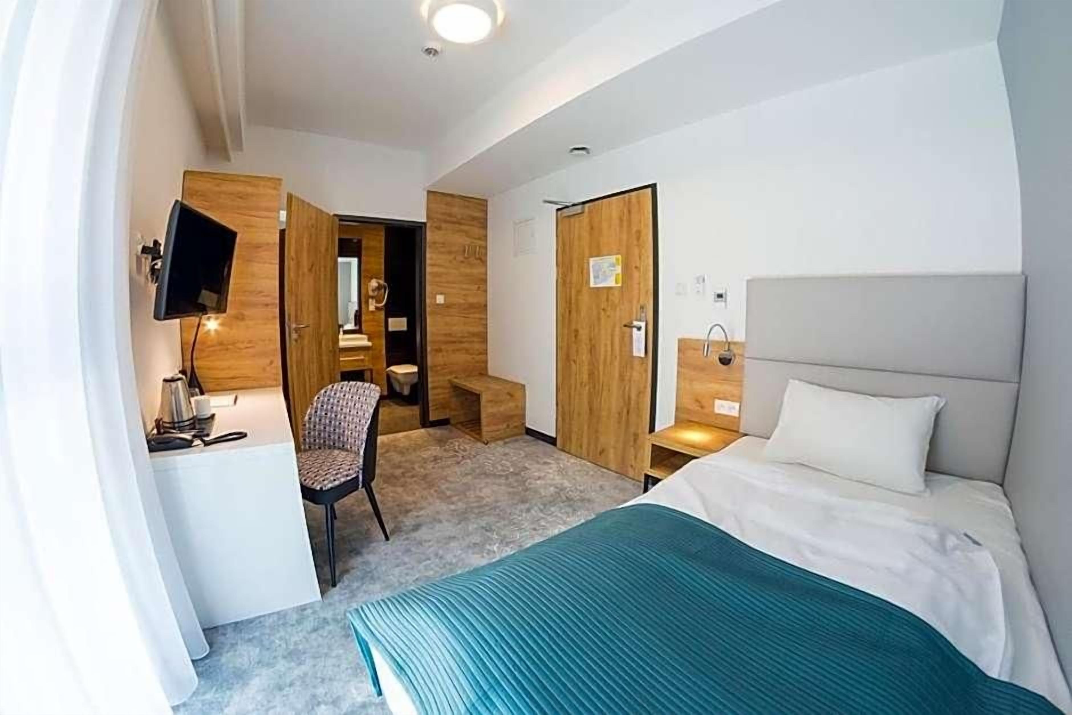 A hotel room with a bed, a desk, a chair, a TV, and a wardrobe.