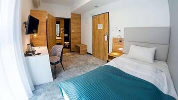 A hotel room with a bed, a desk, a chair, a TV, and a wardrobe.