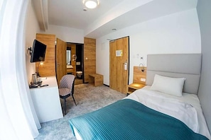 Quarto de hotel com cama, escrivaninha, cadeira, televisão e armário.