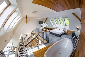Um interior moderno com um grande claraboia, escada, quarto com cama grande e banheira.