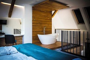 Quarto moderno com cama grande, banheira separada e área de trabalho.