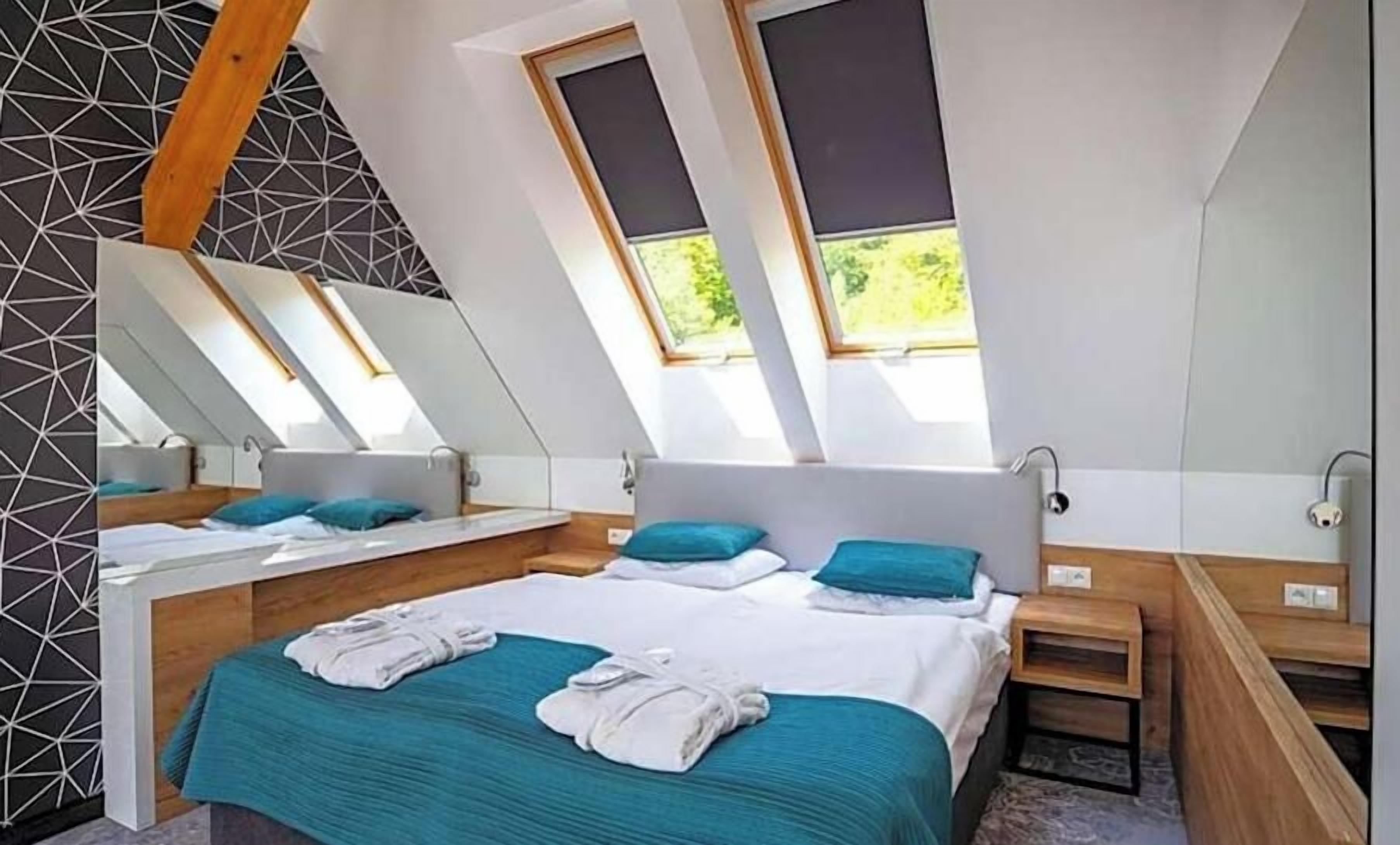 A modern bedroom with a sloped ceiling, skylights, a large bed, bedside tables, and a mirror.