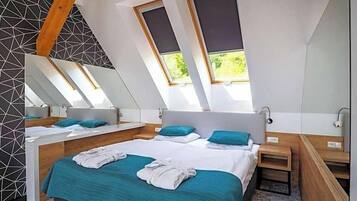 A modern bedroom with a sloped ceiling, skylights, a large bed, bedside tables, and a mirror.