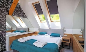 Quarto moderno com teto inclinado, claraboias, cama grande, mesas de cabeceira e espelho.