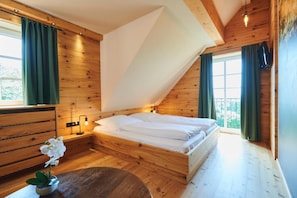 A bedroom with a wooden ceiling, a bed with white linens, a nightstand with a lamp, and a window with curtains. - Hotel Agnesen Hof (Barweiler)