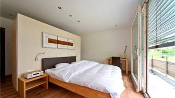 A modern bedroom with a large bed, bedside tables, a wall-mounted artwork, and a sliding glass door leading to an outdoor area.