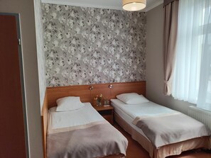 Habitación de hotel con dos camas individuales, cabecero de madera, papel tapiz floral y una ventana con cortinas.