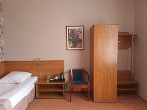 Una habitación de hotel con cama, una silla, un escritorio, un armario y un cuadro en la pared.