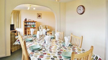 A dining area with a table set for four, a bookshelf, and a clock on the wall.