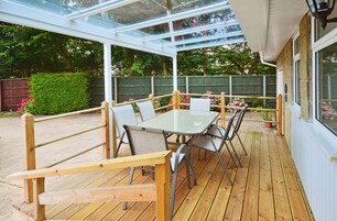 A covered patio with a table and chairs, surrounded by a wooden deck and a glass enclosure.