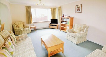 A living room with a sofa set, a coffee table, a television, and a bookshelf.