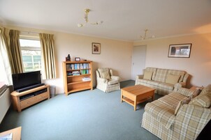A living room with a television, bookshelf, armchair, sofa, and coffee table.