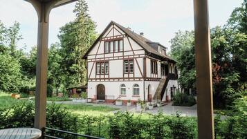 A traditional half-timbered house with a staircase leading to the entrance, surrounded by lush greenery.