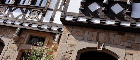A half-timbered building with a stone base, multiple windows, and a small balcony with statues.