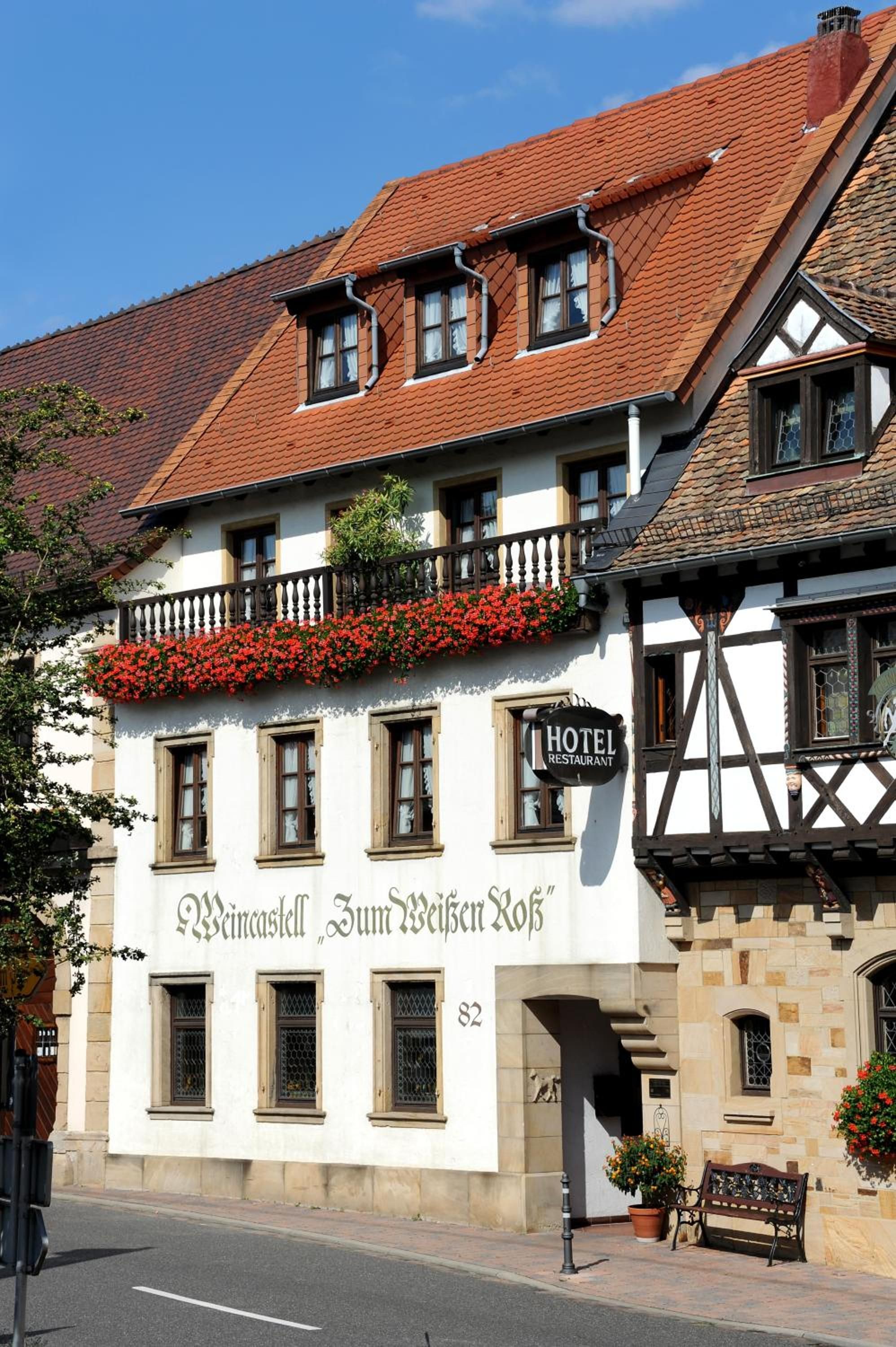 A traditional building with a sign 'Hotel Restaurant Zum Weißen Roß' and a balcony with red flowers.