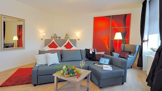 A modern living room with a grey sofa, a coffee table with a floral arrangement, a laptop, and a chair. - Landhaus Heidekrug (Diekholzen)