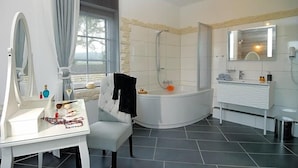 A modern bathroom with a bathtub, a vanity with a mirror, and a window providing a view. - Landhaus Heidekrug (Diekholzen)
