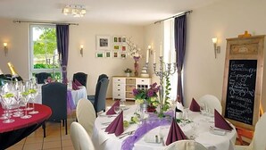 A dining area with round tables set for a meal, a chalkboard menu, and a view of the outdoors. - Landhaus Heidekrug (Diekholzen)