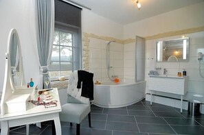 A modern bathroom with a bathtub, a vanity with a mirror, and a window providing a view. - Landhaus Heidekrug (Diekholzen)