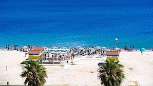 A beach with several structures, including a building with a red roof and a smaller structure with a blue roof, both on the sand near the water. - Hotel Poseidon (Corigliano-Rossano)