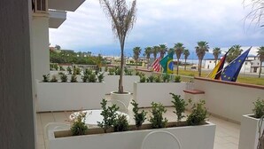 An outdoor terrace with a white table and chairs, surrounded by planters and palm trees. - Hotel Poseidon (Corigliano-Rossano)