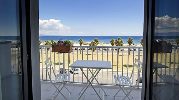 A balcony with a view of the beach, white chairs, and a table. - Hotel Poseidon (Corigliano-Rossano)