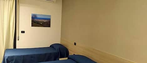 A hotel room with two beds, a window with curtains, an air conditioning unit, and a wall-mounted picture.